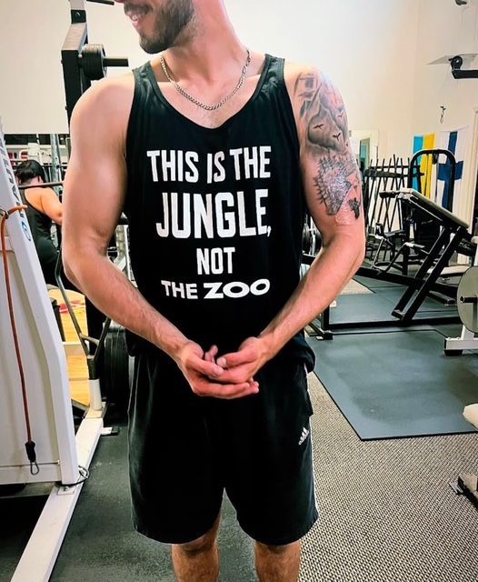 Man in gym flexing biceps, wearing a tank top that says 