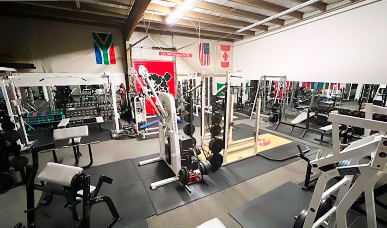 Gym interior with weight machines, benches, and free weights; flags hang on the wall.