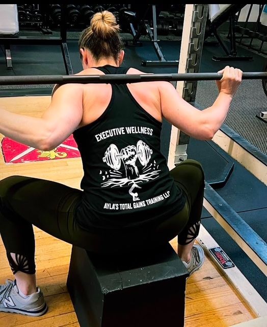 Woman doing box squat with barbell at the gym, wearing a tank top with logo.