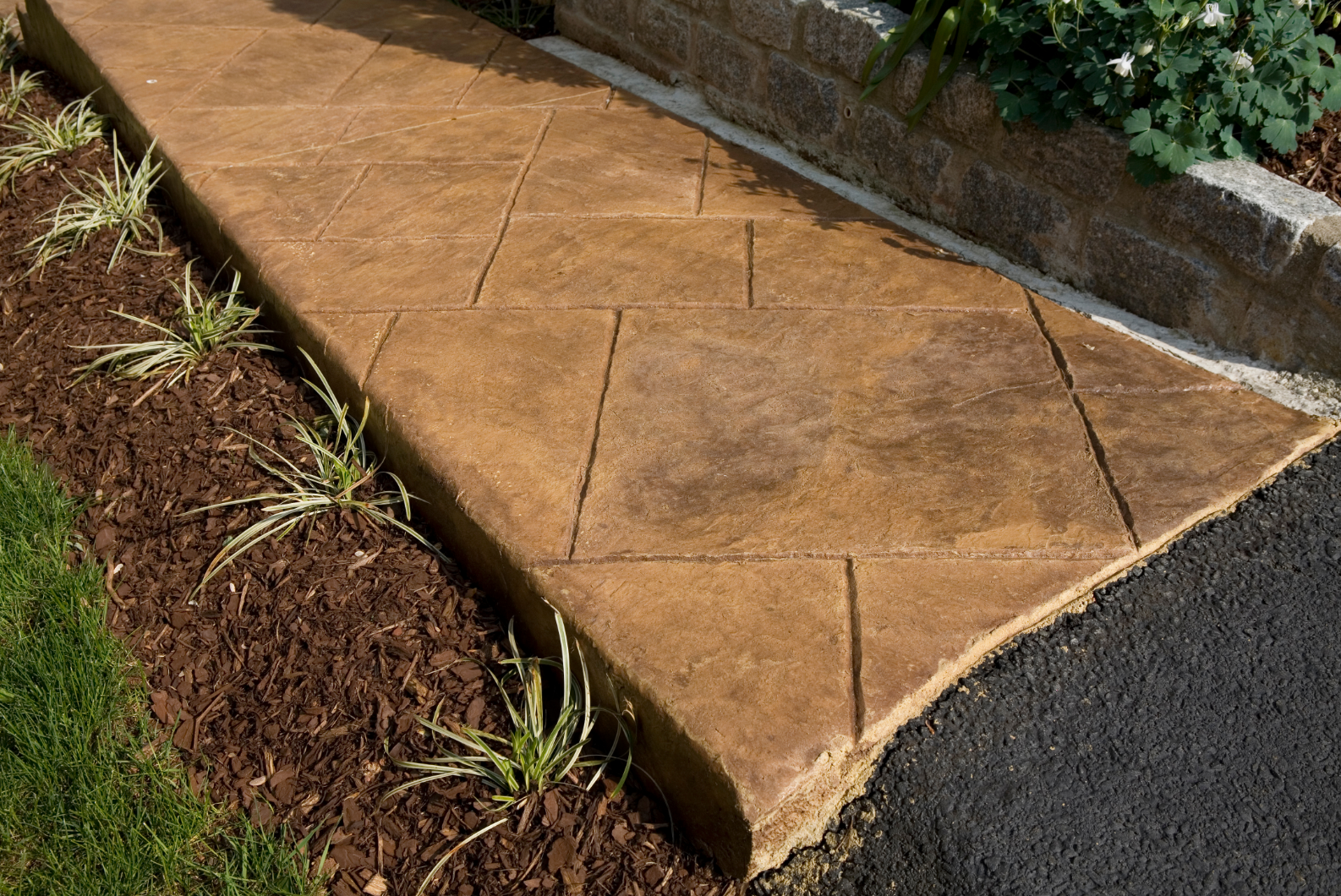 Picture of a stamped concrete walkway in a backyard.  The concrete is tinted and has a nice texture.  The walkway travels through two gardens on either side.