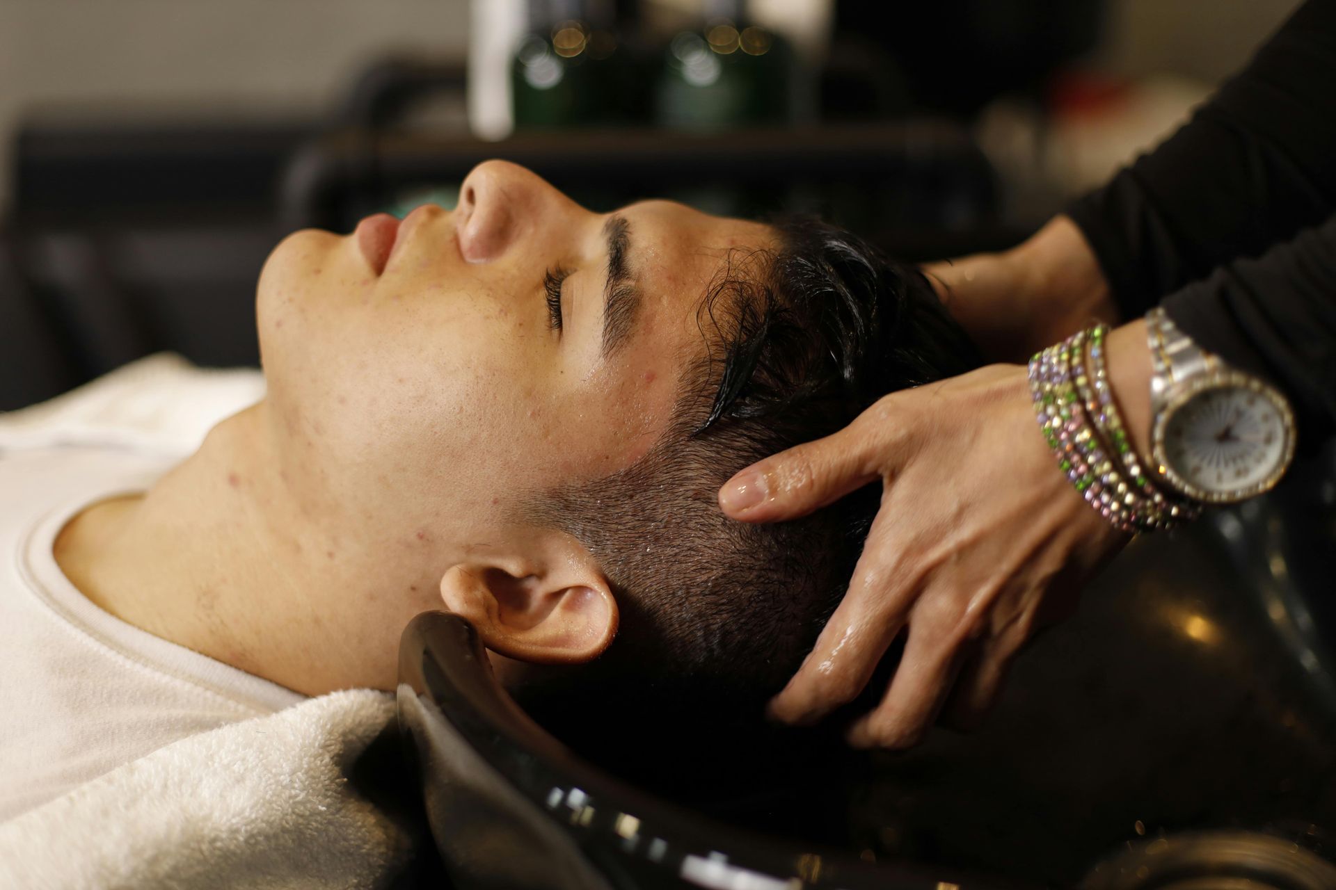 Man getting his hair washed at a salon; person's hands massaging his head.