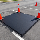 Fresh black asphalt patch in a parking lot, marked off by orange traffic cones