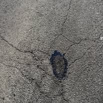 Worker in hard hat and orange vest repairing cracked asphalt in a parking lot.