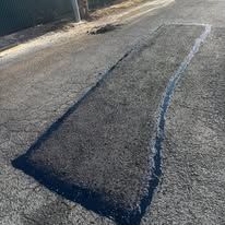 Cracked black asphalt road with a long central fissure and orange cones in the distance