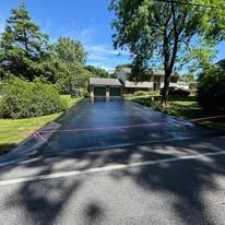 Freshly paved dark asphalt driveway between curbs and landscaped lawns in a residential area