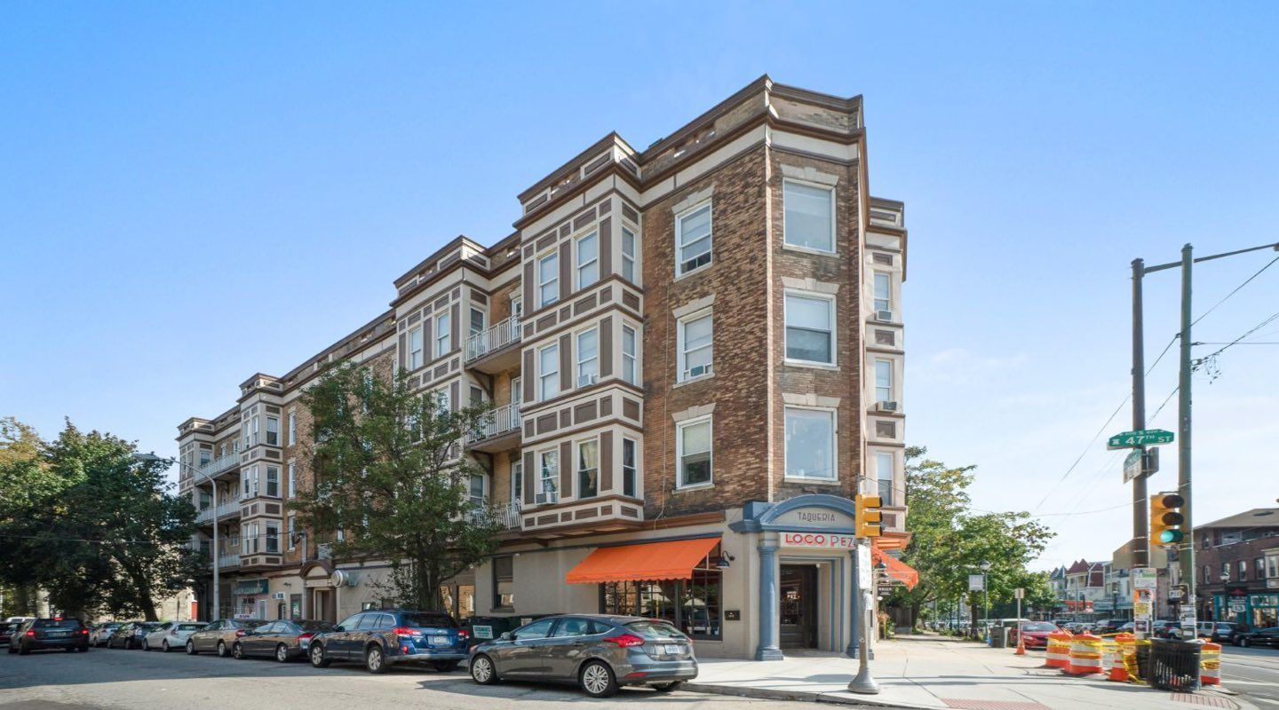Photo of a large multi-story building seen from across the street. It's triangular in footprint and is at a city corner