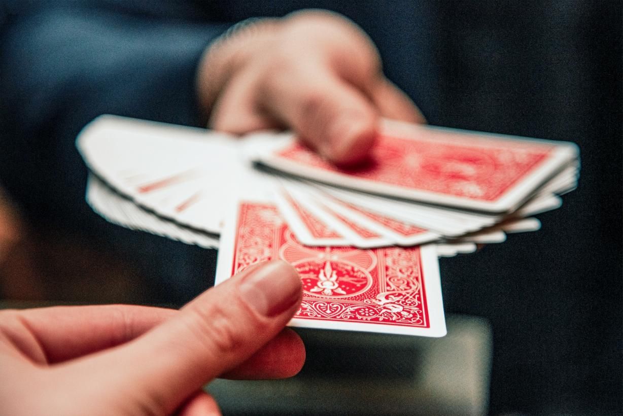 Hands fanning a deck of red-backed playing cards on a dark background