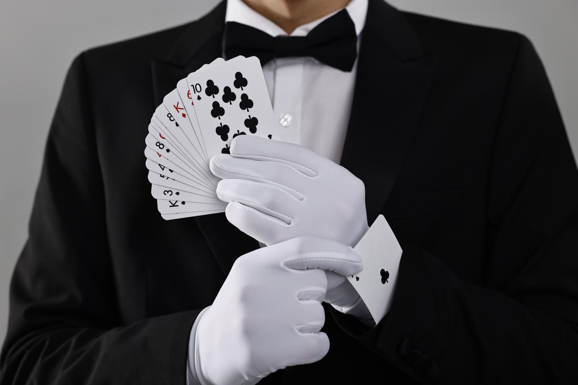 Magician in black tuxedo and white gloves fanning playing cards against a dark background