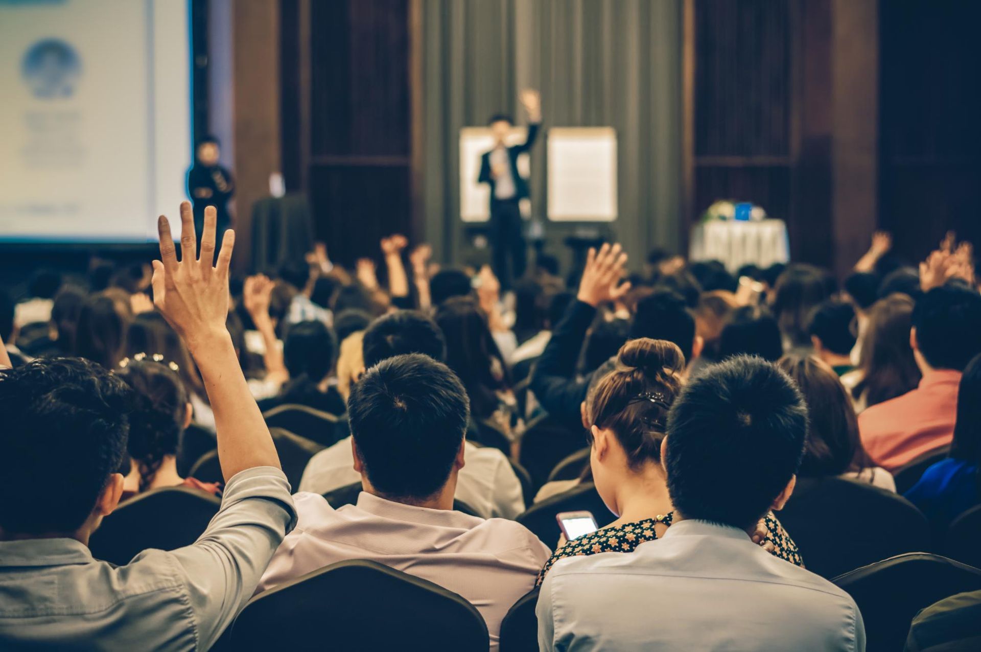 Audience raising hands during a conference presentation in a large auditorium