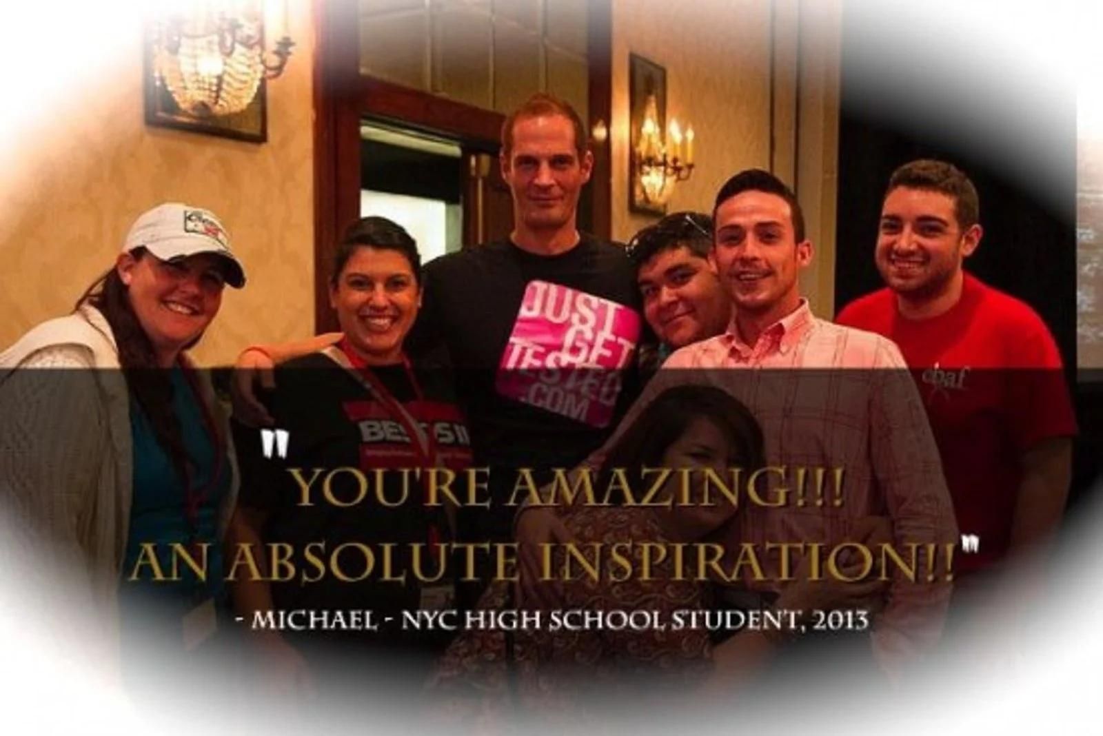 Five smiling people posing indoors with a framed quote in the foreground
