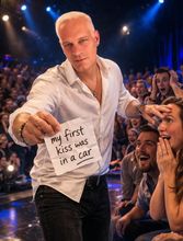Daniel Bauer holds a note reading “my first kiss was in a car” toward a cheering crowd