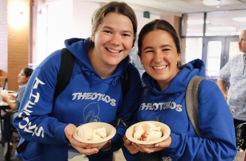 Two smiling people wearing matching blue hoodies holding paper bowls of food.
