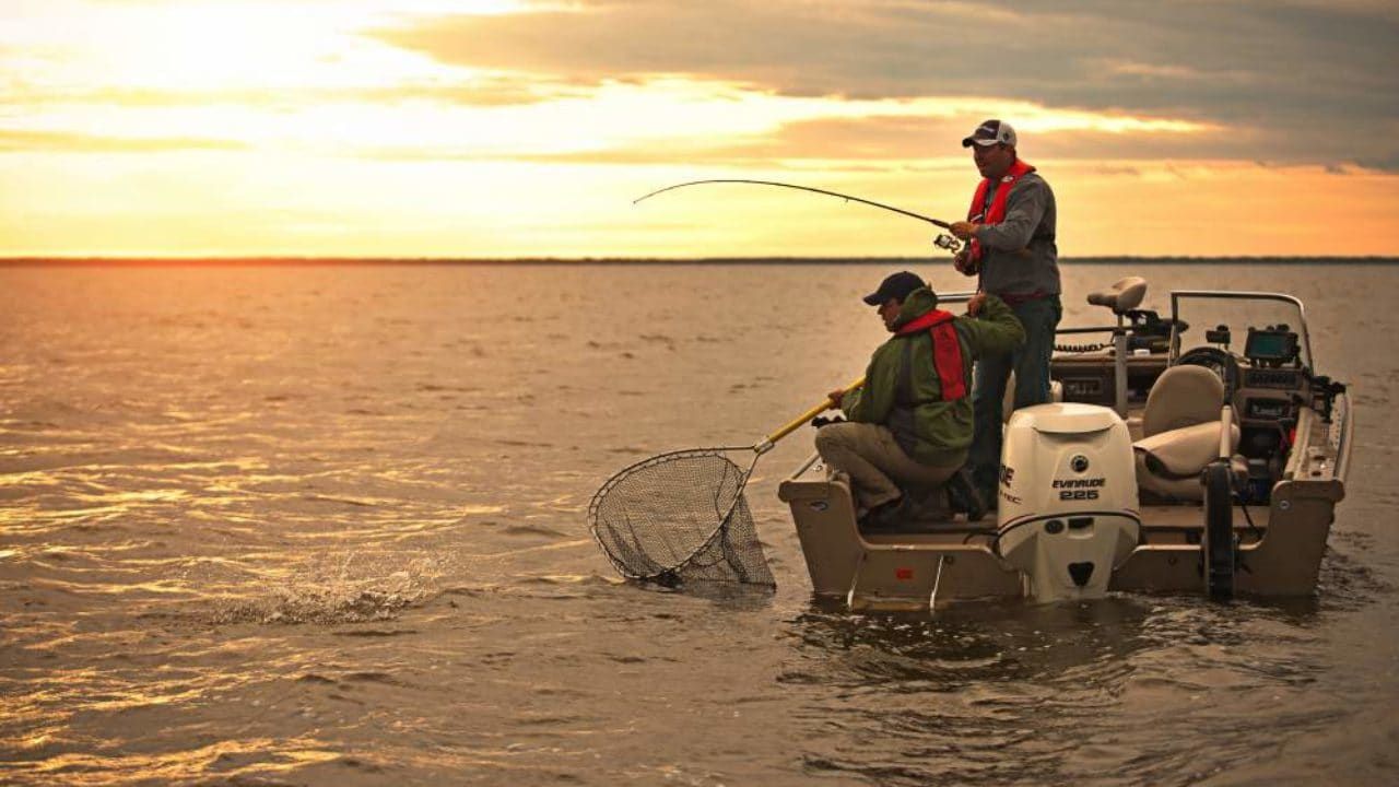 Two men are fishing on a rock near the ocean at sunset.