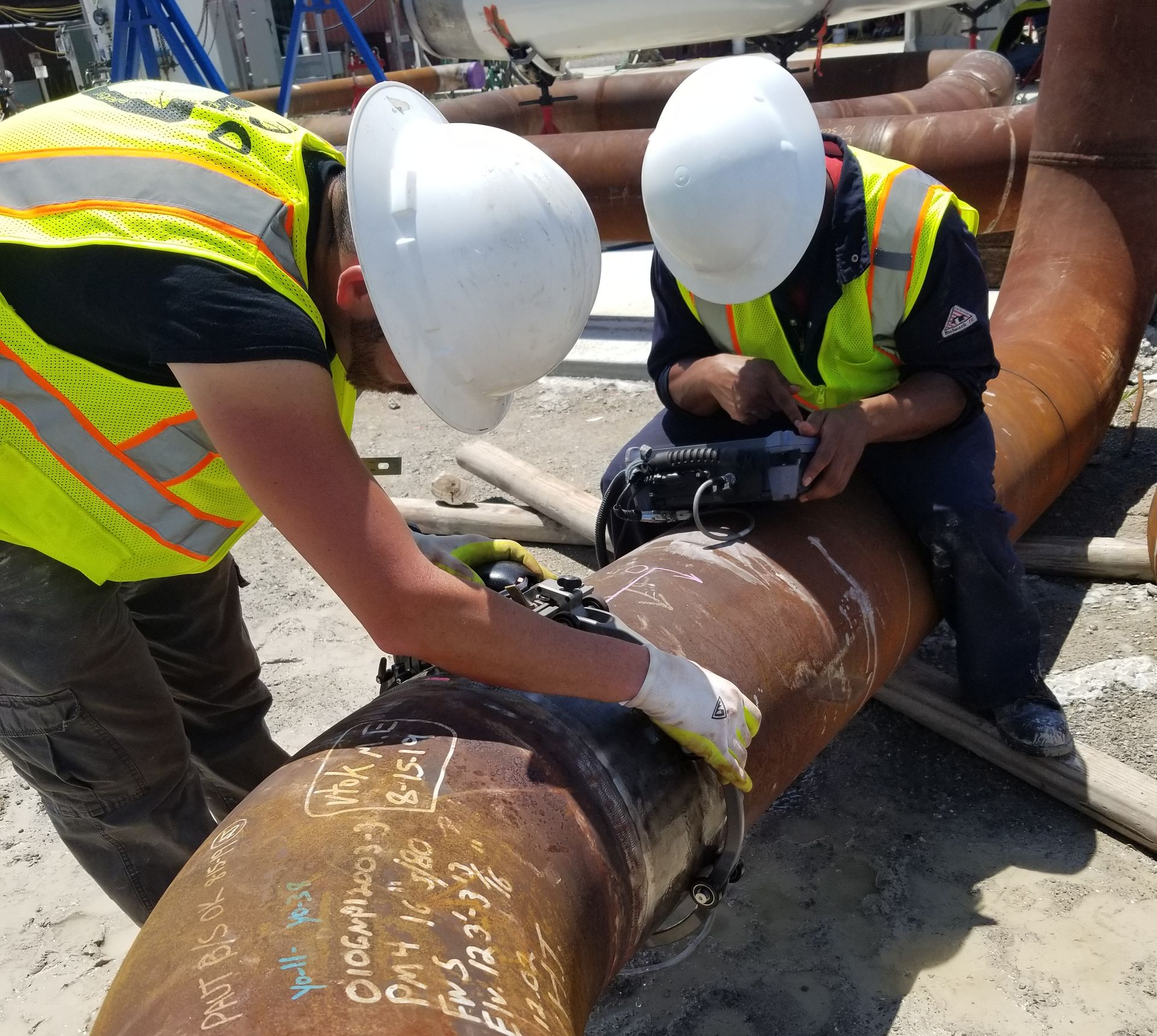 Workers in hard hats inspect and weld a large rust-colored pipe at a construction site