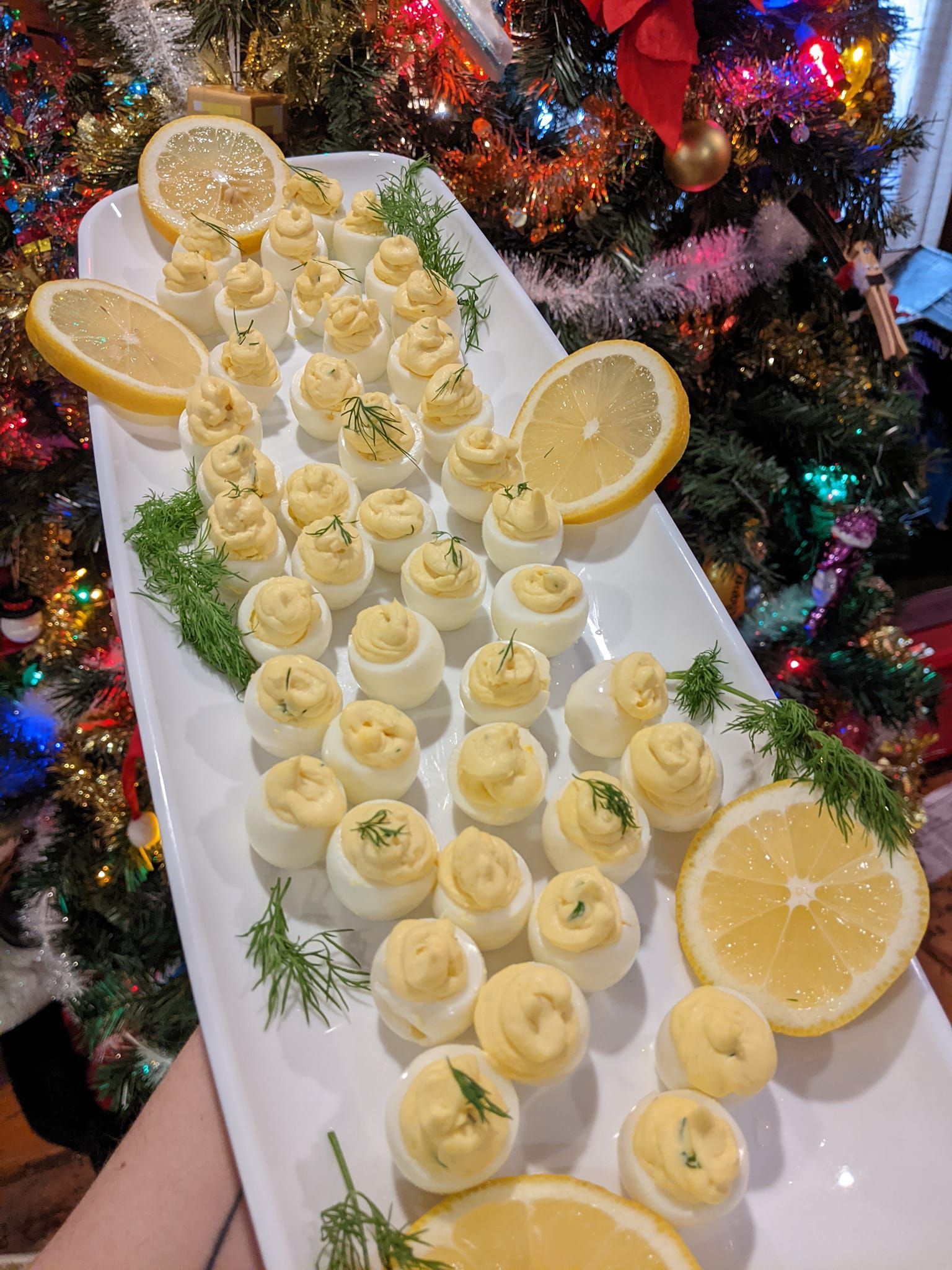 A person is holding a plate of food with lemon slices in front of a christmas tree.