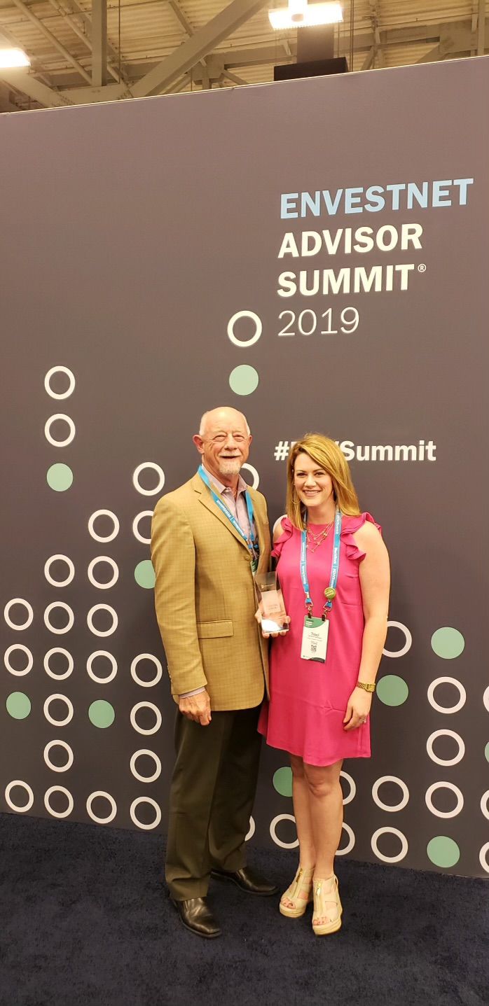 A man and a woman are posing for a picture in front of a wall that says investnet advisor summit 2019.