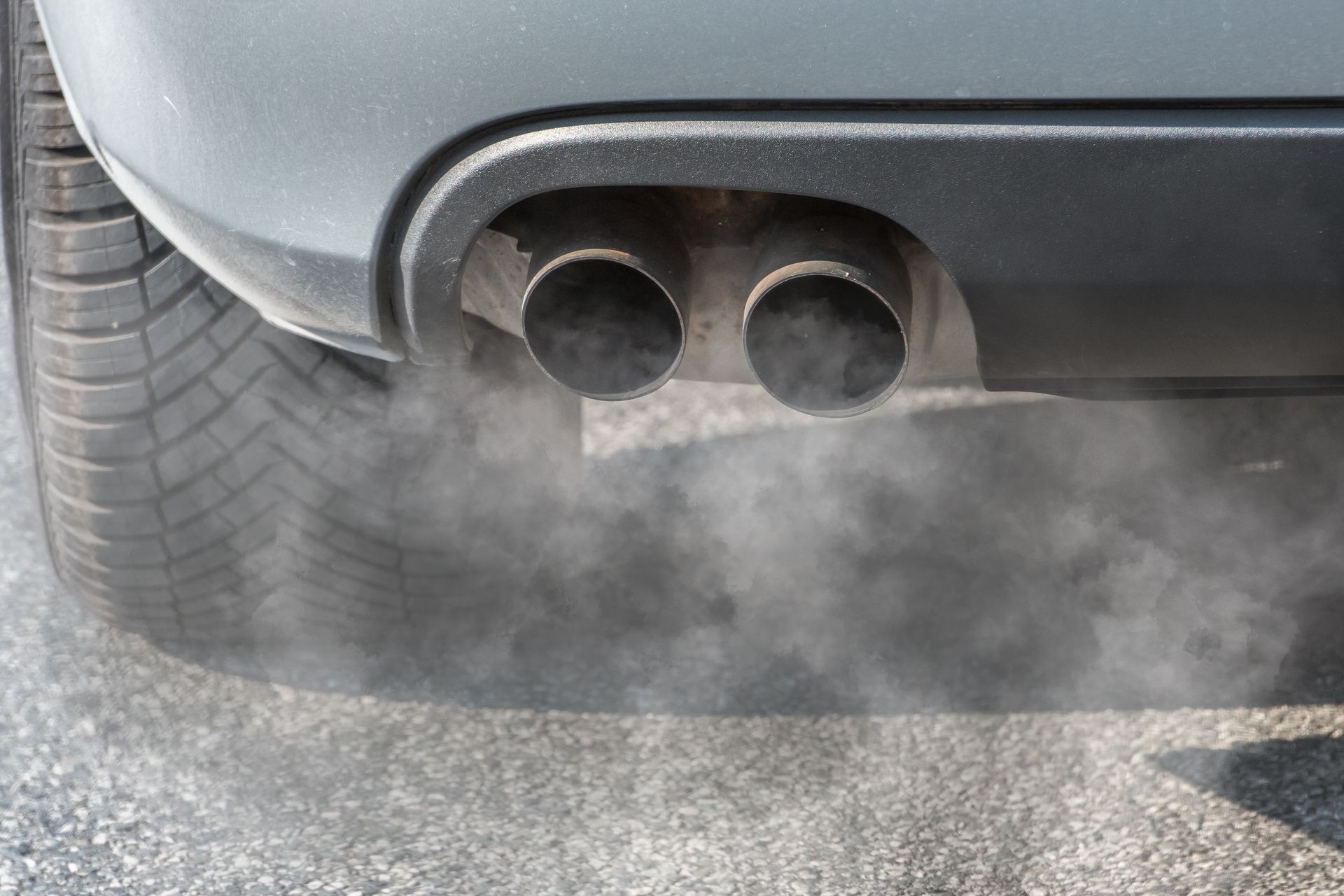Rear of a gray car with dual exhaust pipes emitting visible exhaust smoke | Quality Auto Repair Tire & Auto Sales