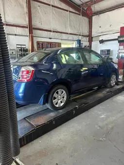 Blue sedan on a car lift inside an auto repair shop. | Quality Auto Repair Tire & Auto Sales