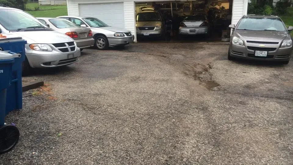 Several parked cars line a gravel driveway in front of an open garage. | Quality Auto Repair Tire & Auto Sales