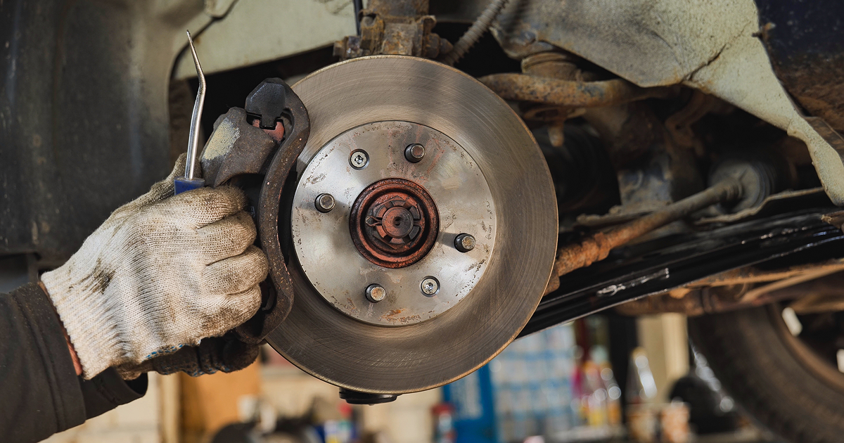 Mechanic holding brake rotor and caliper during vehicle repair in a garage | Quality Auto Repair Tire & Auto Sales