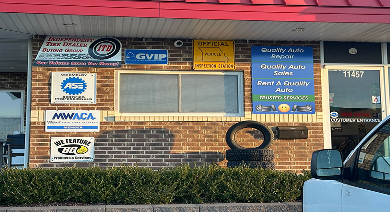 Brick storefront with multiple signs, blue awning, and a person standing at the left edge | Quality Auto Repair Tire & Auto Sales