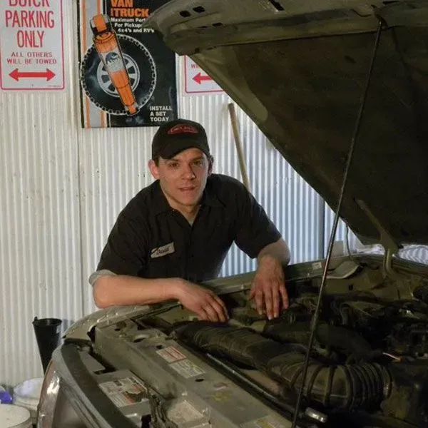 Mechanic leaning over an open car hood in a garage, inspecting the engine | Quality Auto Repair Tire & Auto Sales