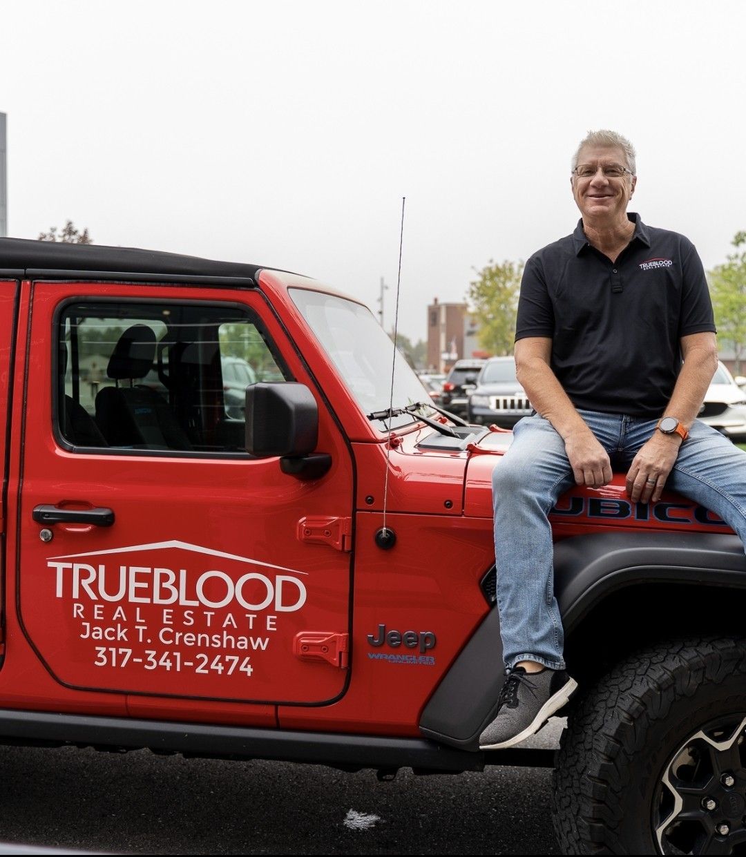 Man sits on the hood of a red Jeep with 