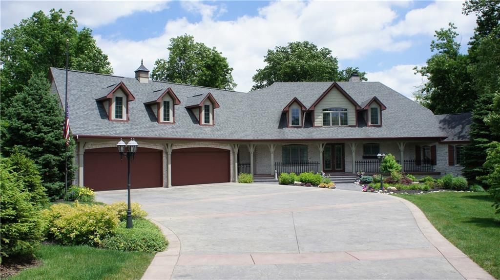 Large beige house with gray roof, three dormers, two-car garage, and long driveway.