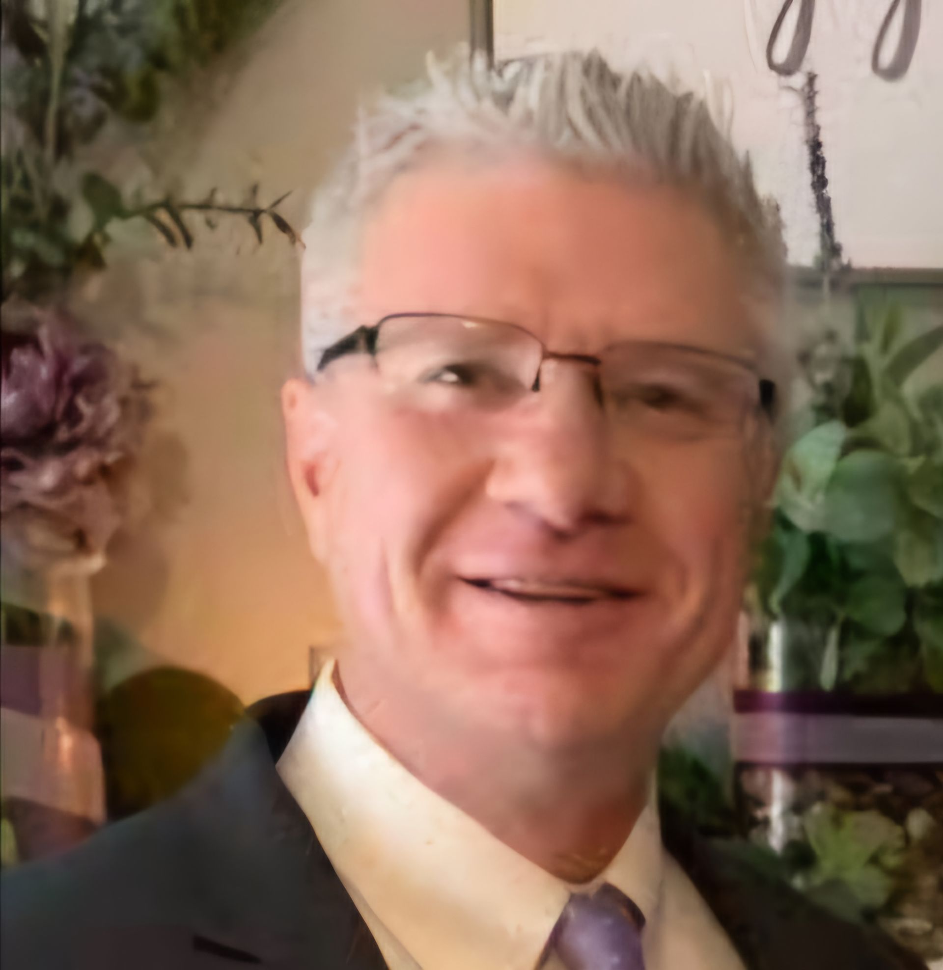 Man with gray hair and glasses smiling, wearing a suit jacket and tie.