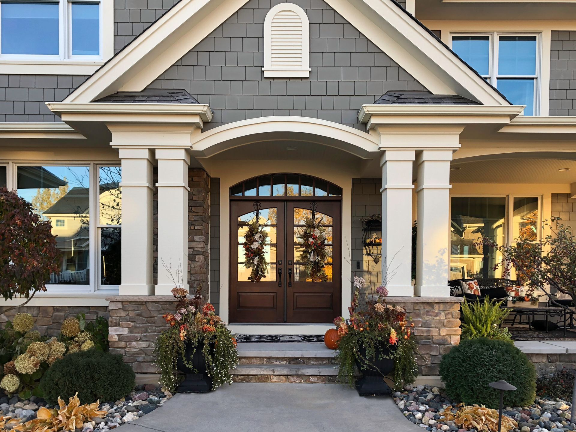 Front exterior of a house with stone accents, a dark wood door, and fall decorations.