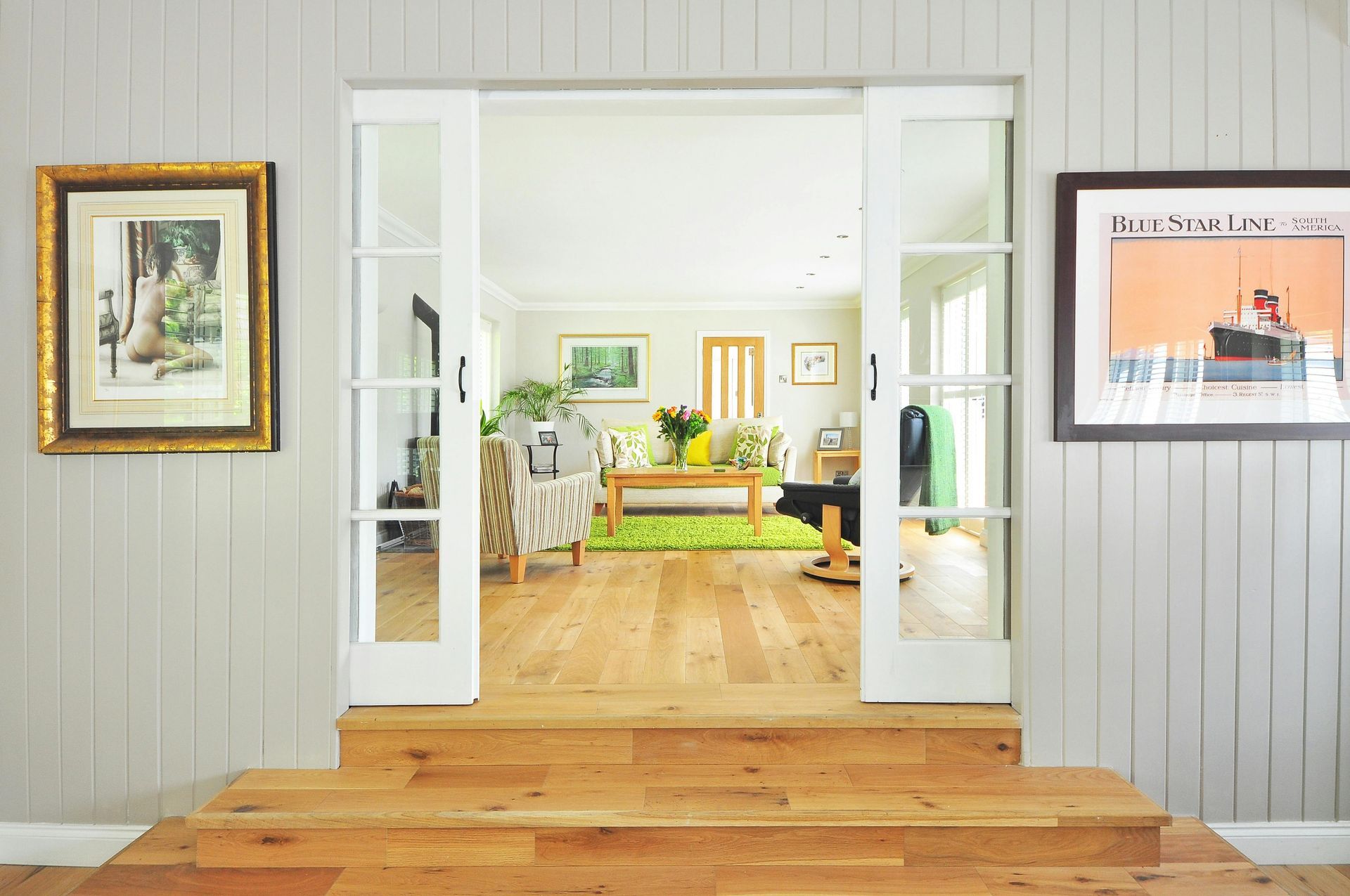 View of a bright living room through open double doors with art on the walls.