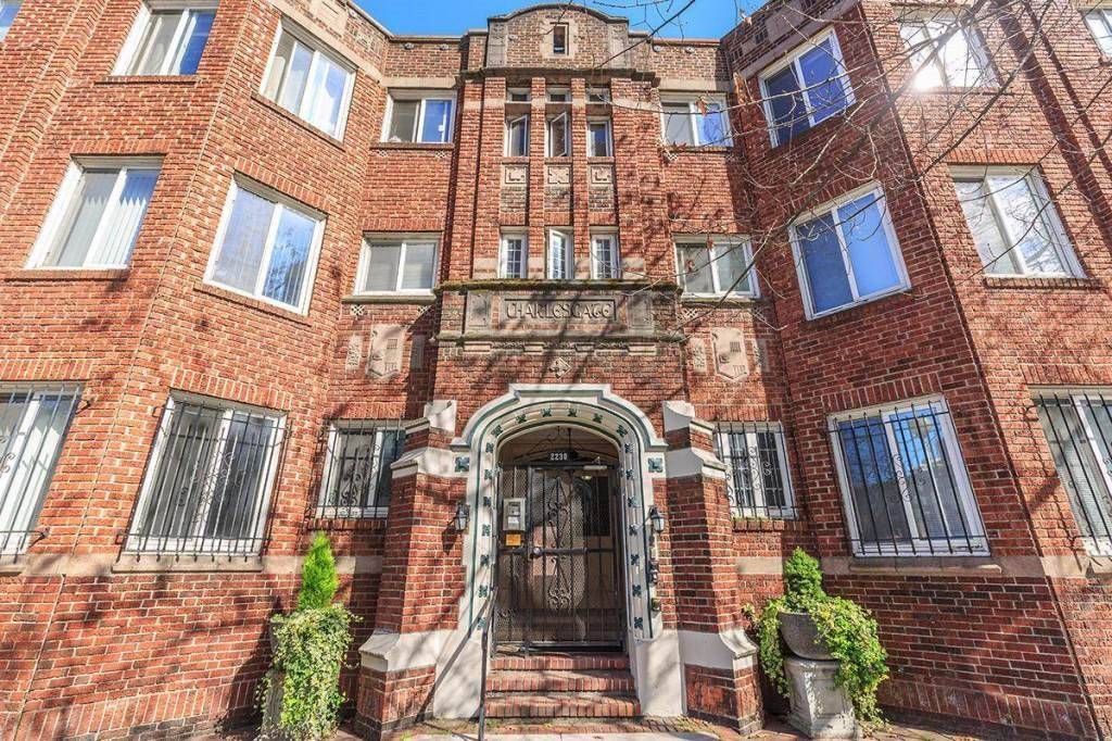 Red brick apartment building with arched entrance and potted plants on the front steps