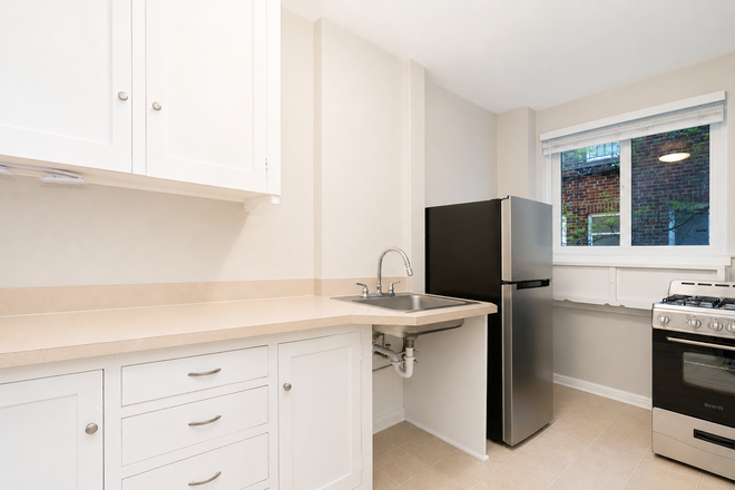 Bright white kitchen with cabinets, countertop, sink, black fridge, and stove by a window.