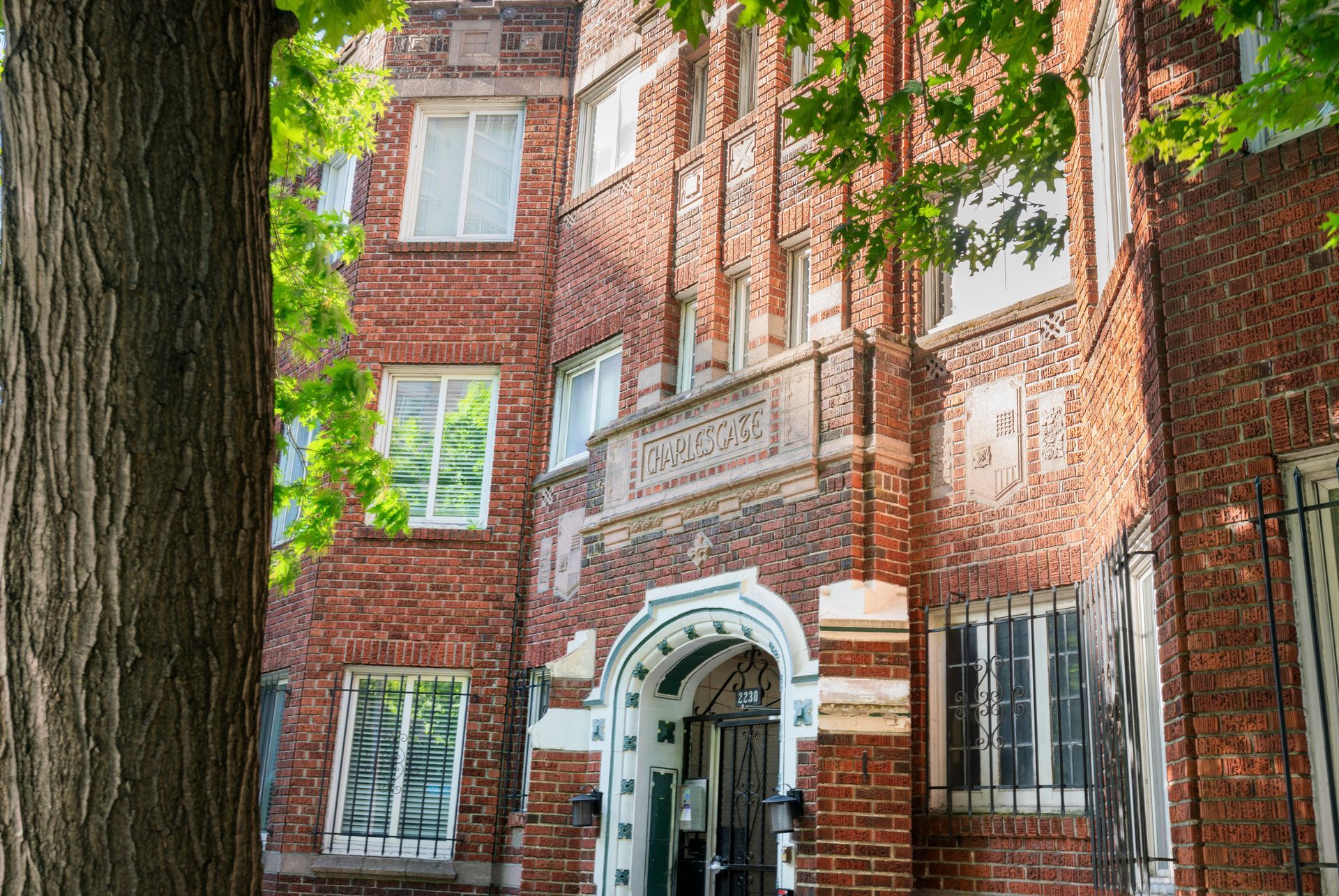Brick apartment building entrance framed by large trees and white-trimmed windows