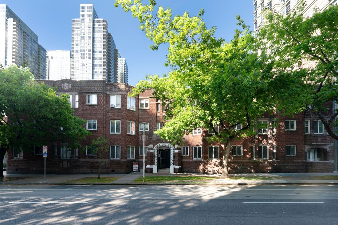 Red-brick apartment buildings shaded by trees on a sunny city street