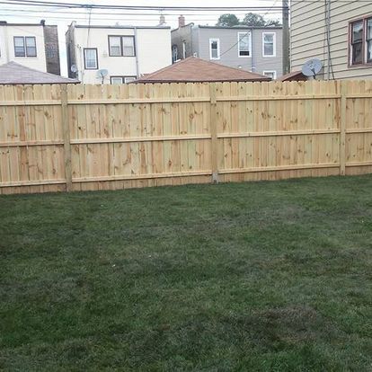 A wooden fence surrounds a lush green lawn in a backyard.
