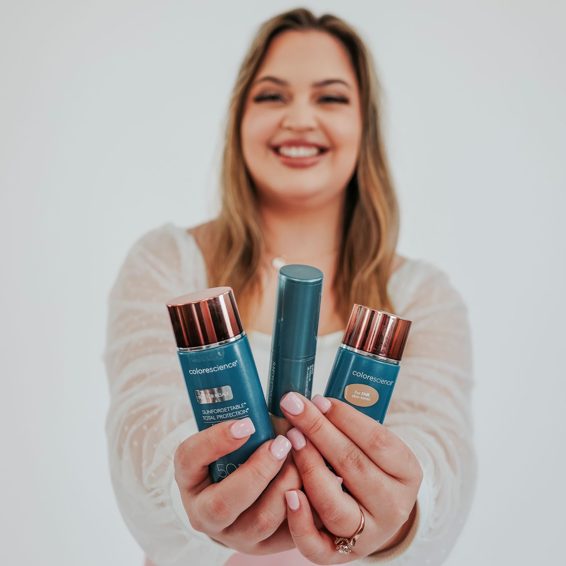 Woman smiling, holding three blue beauty products with rose gold accents.