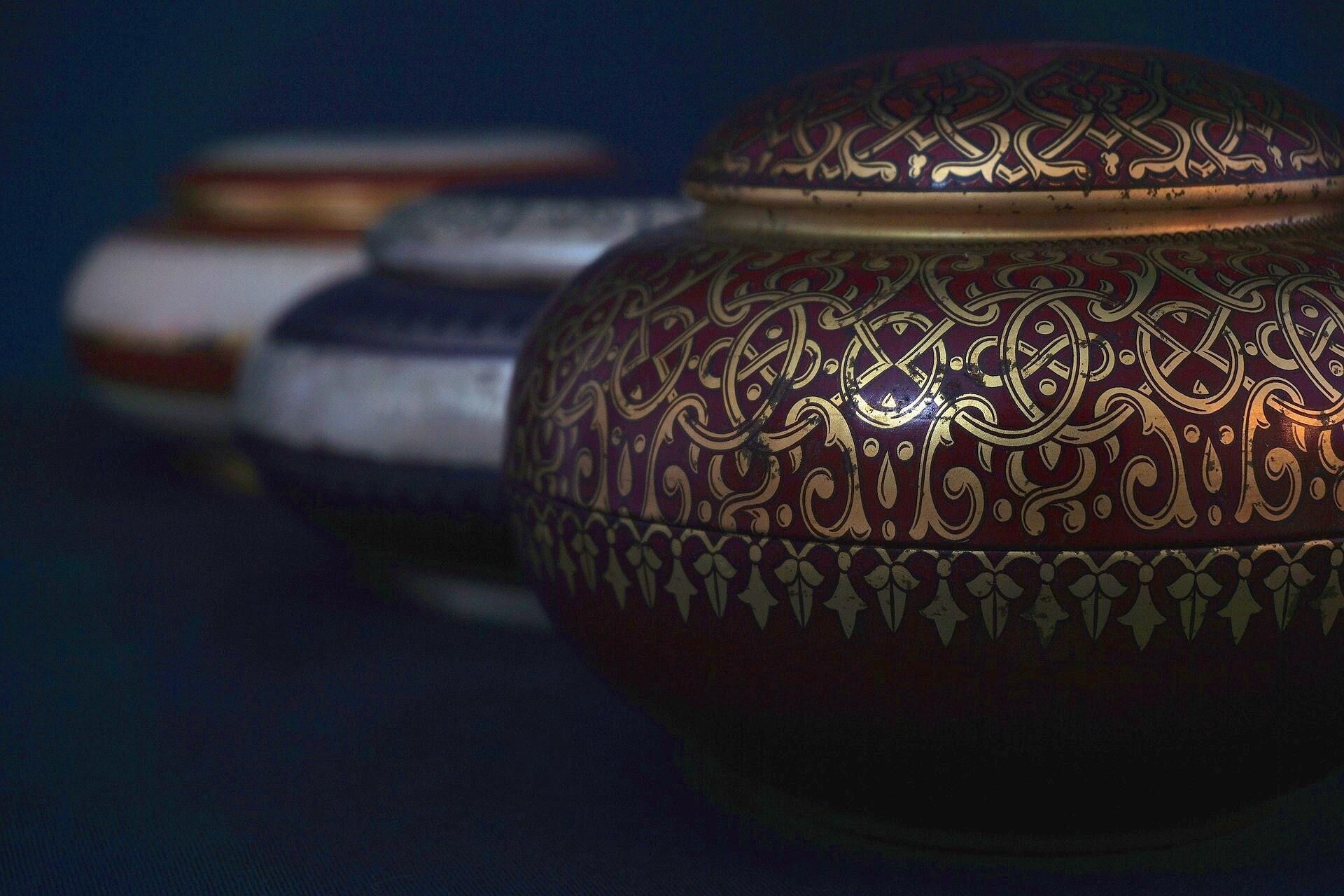 Three ornate, lidded jars. The closest is burgundy with gold patterns; others are white, blue, and gold.