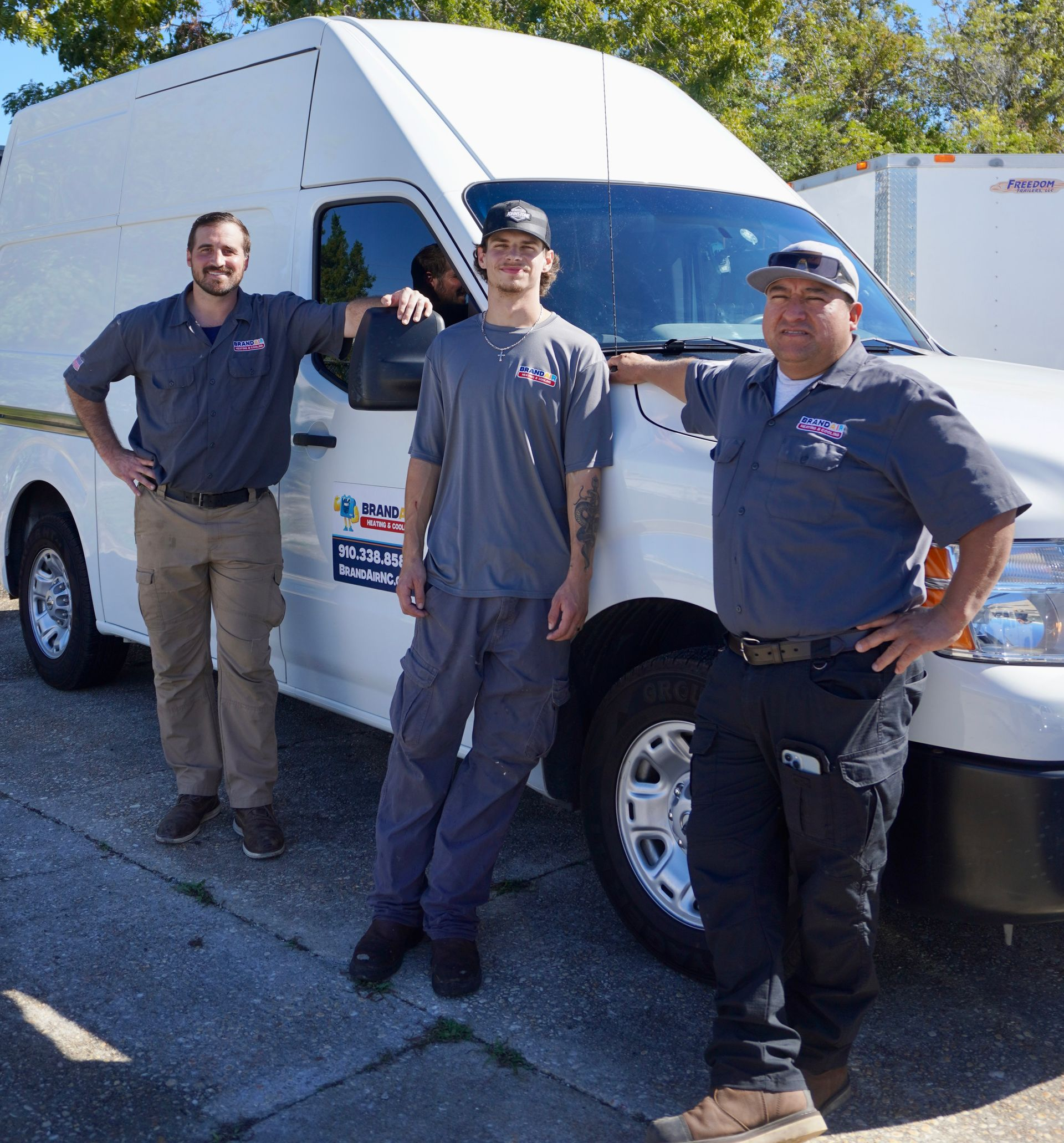 Three workers in navy shirts stand outdoors beside a white truck in bright sunlight.