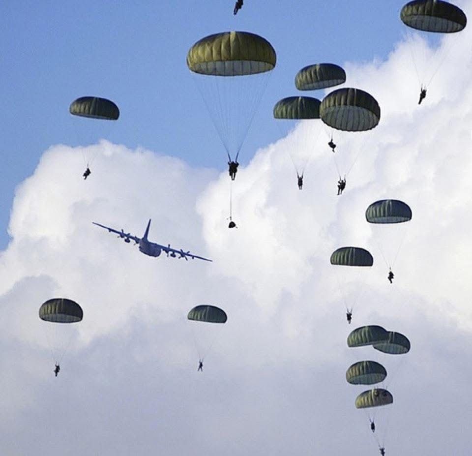 A plane is flying in the sky with parachutes hanging from it