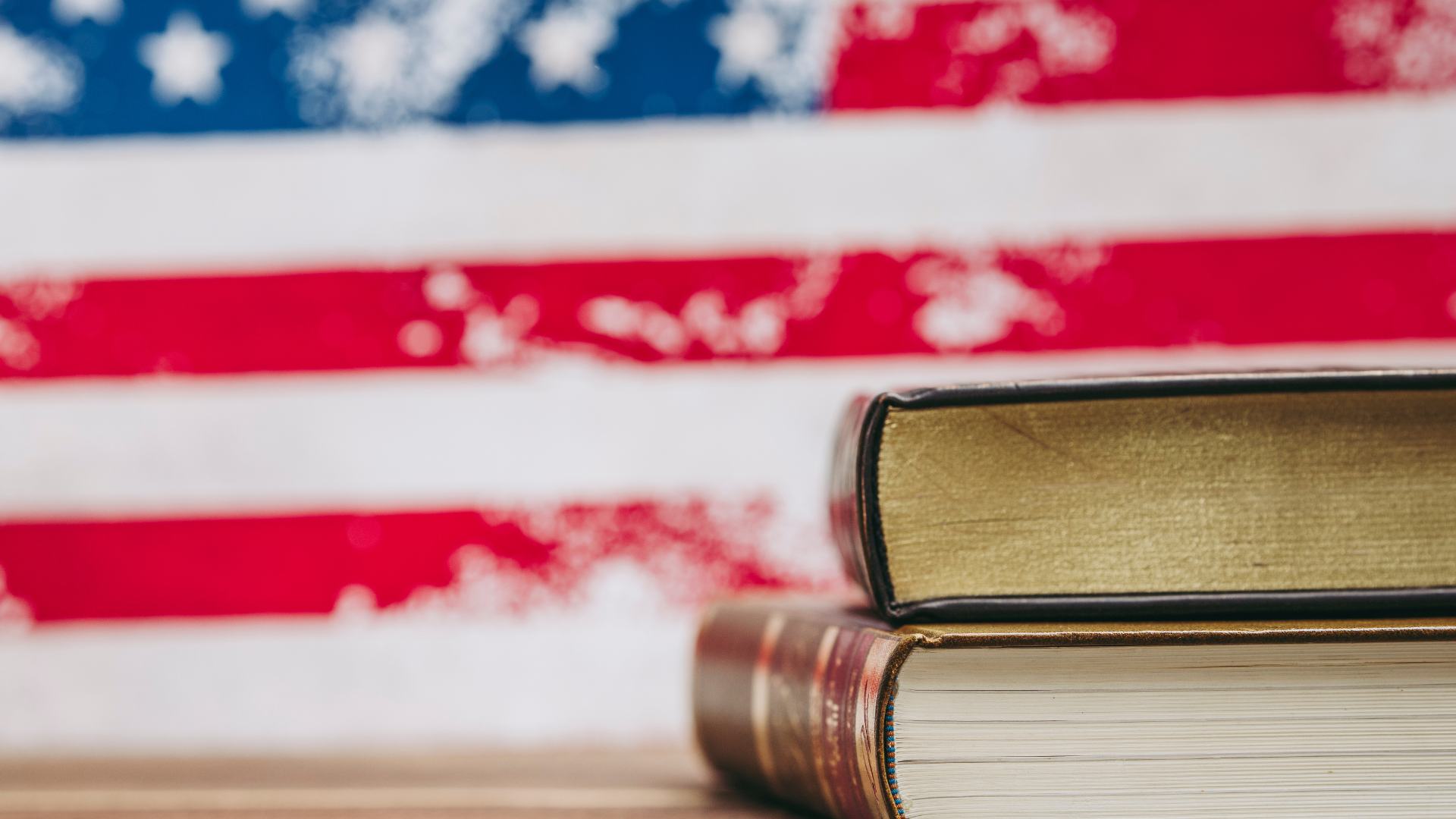 Two stacked books in front of a blurred American flag backdrop