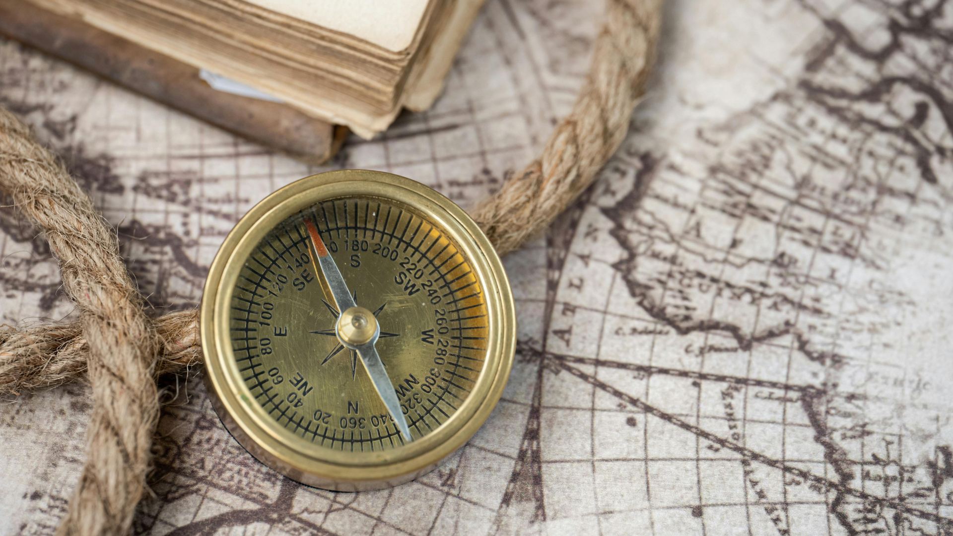 Brass compass on a vintage map beside rope and books, suggesting travel and navigation