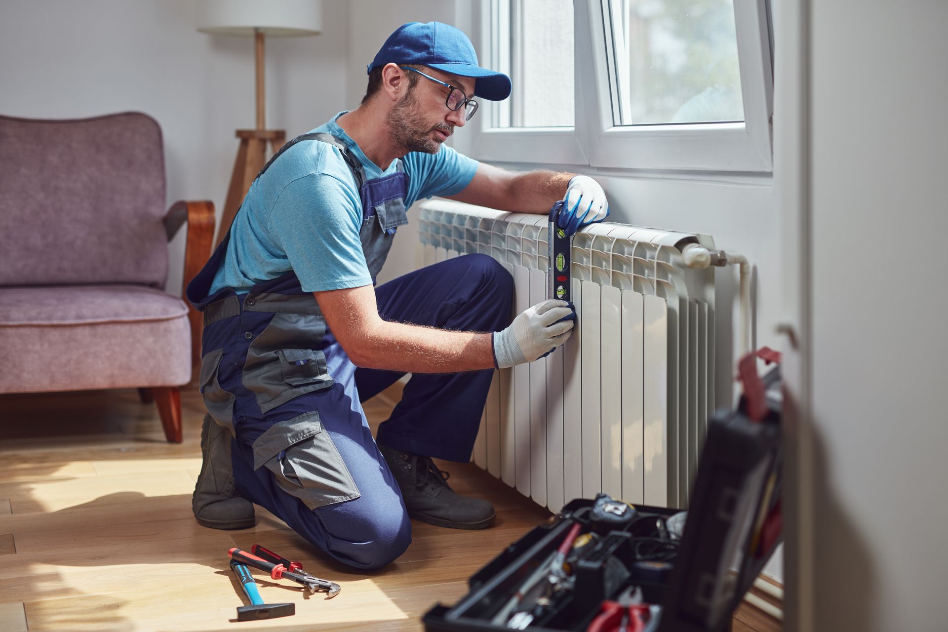 A man is kneeling down fixing a radiator in a living room.