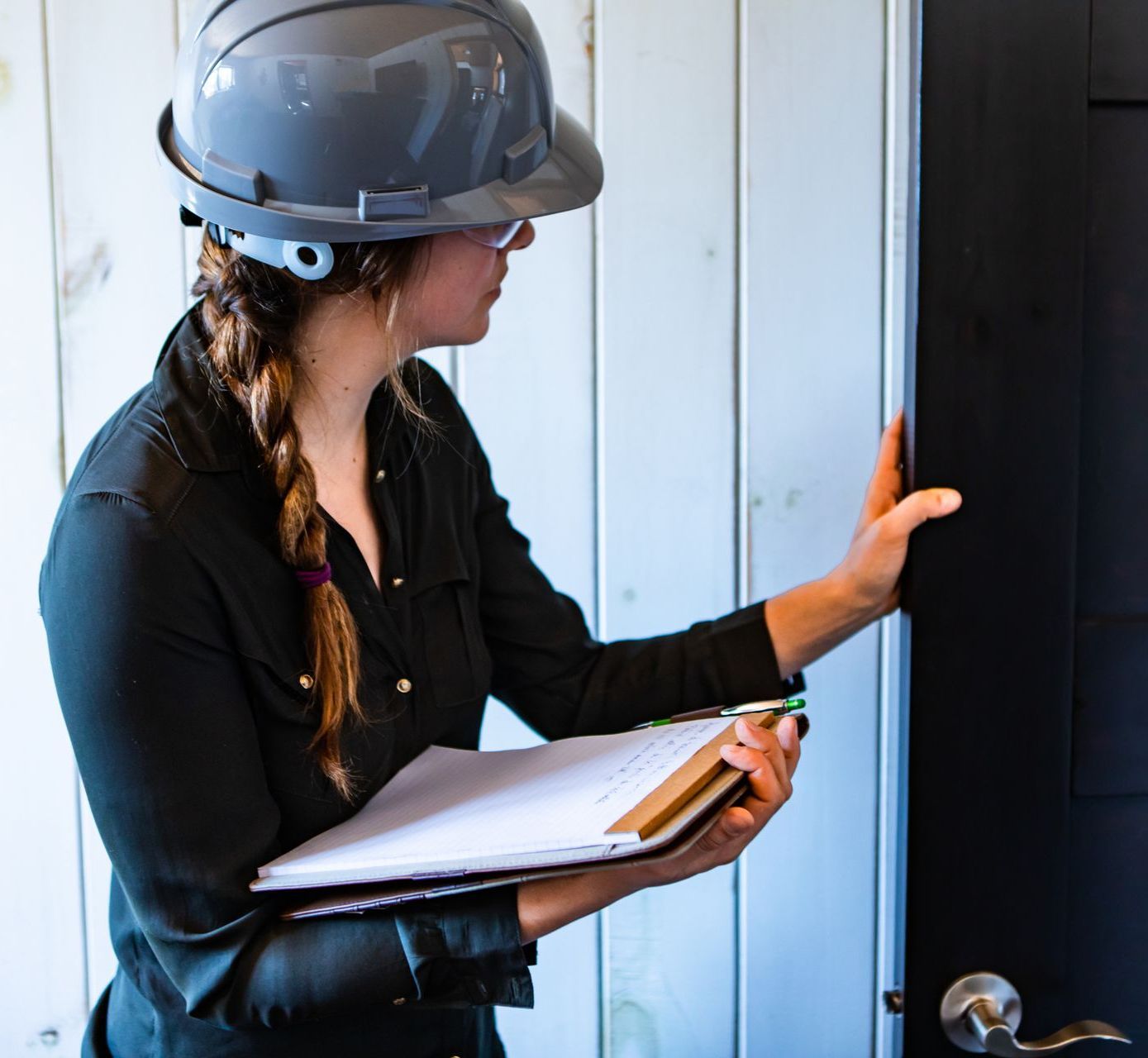 A woman wearing a hard hat is holding a clipboard