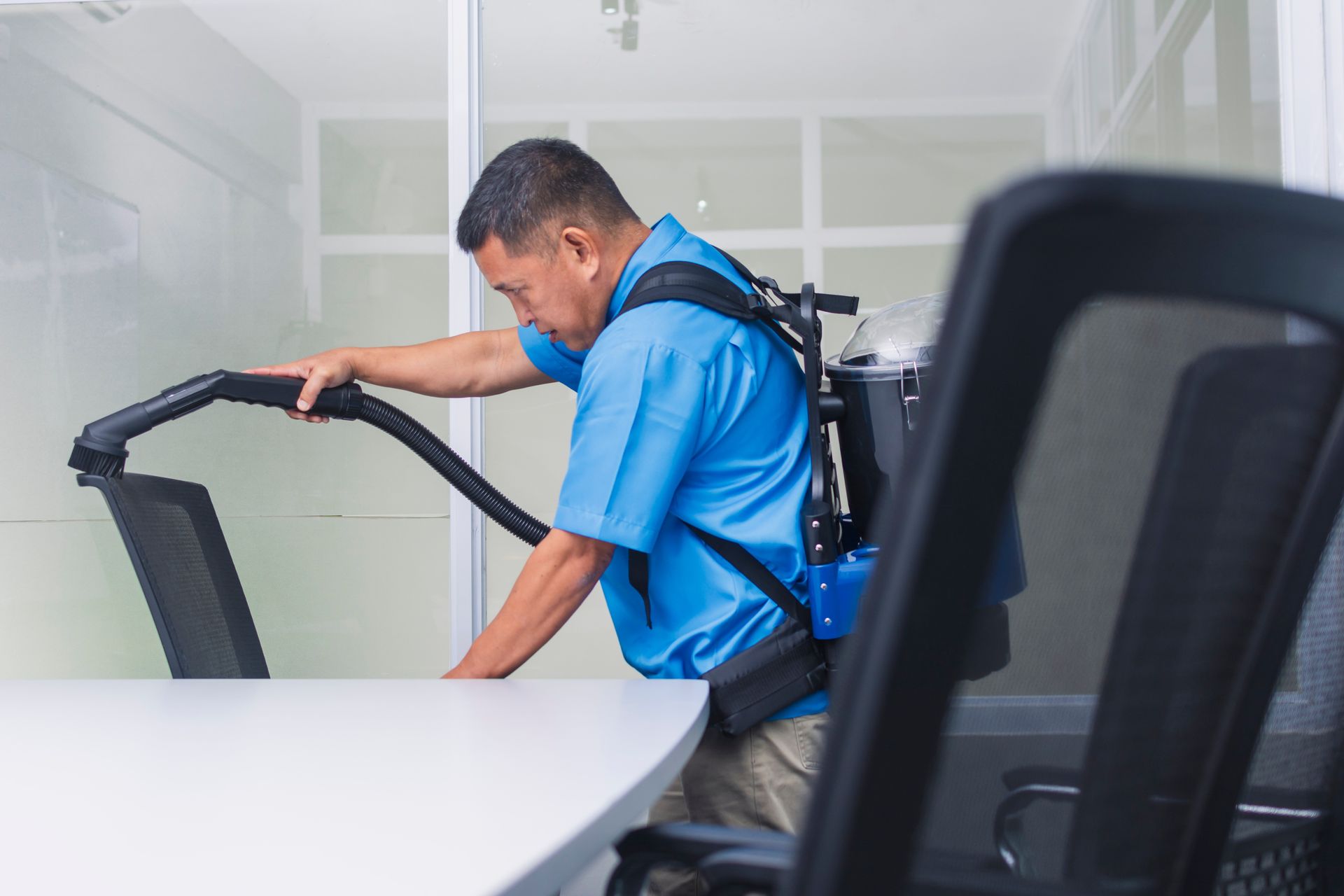 A man is cleaning an office with a backpack vacuum cleaner.