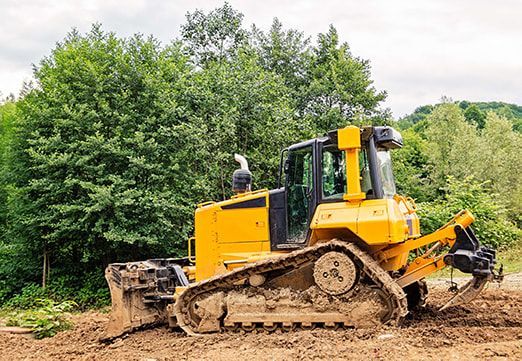 Yellow bulldozer on muddy ground, trees in background.