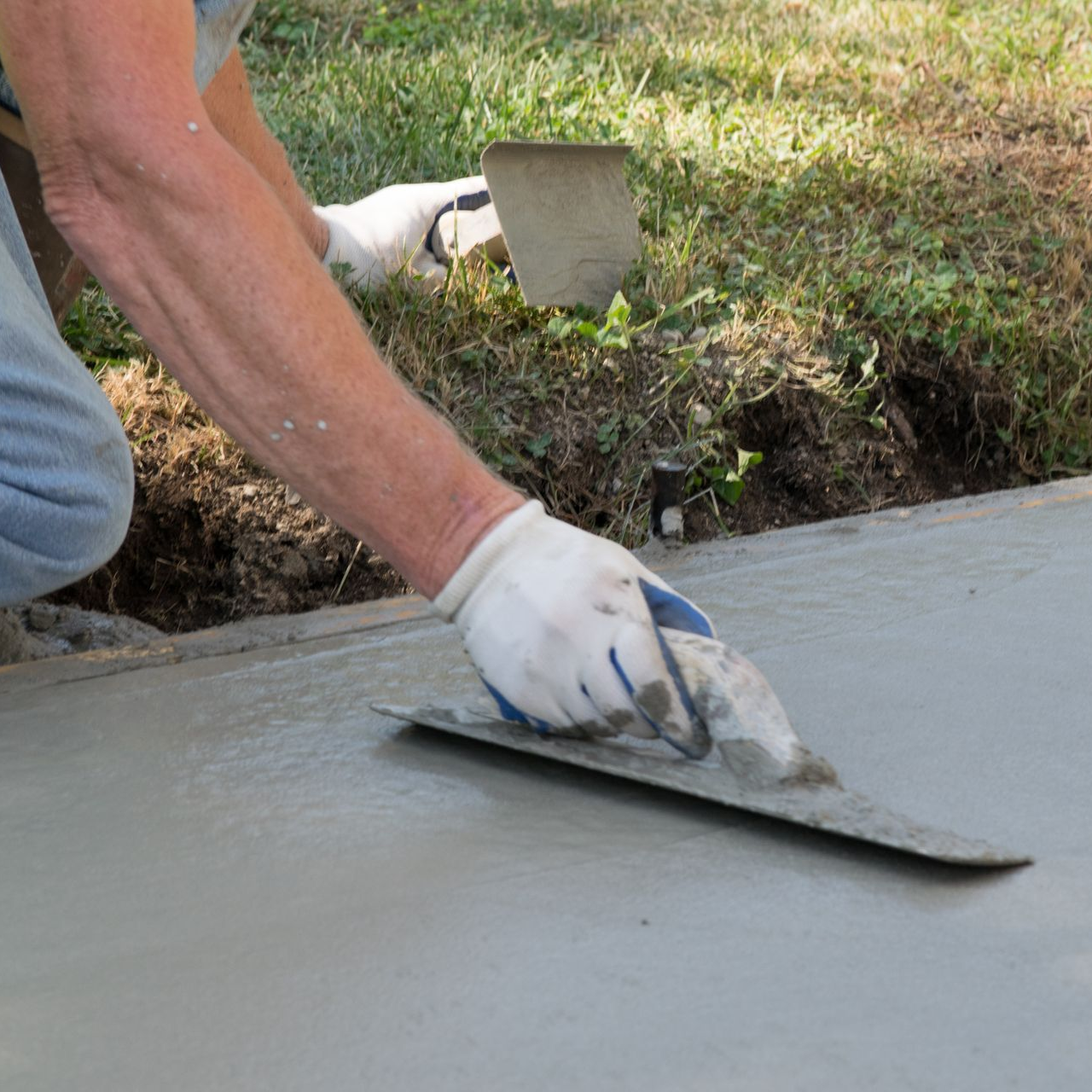 Person smoothing wet concrete with a trowel outdoors.