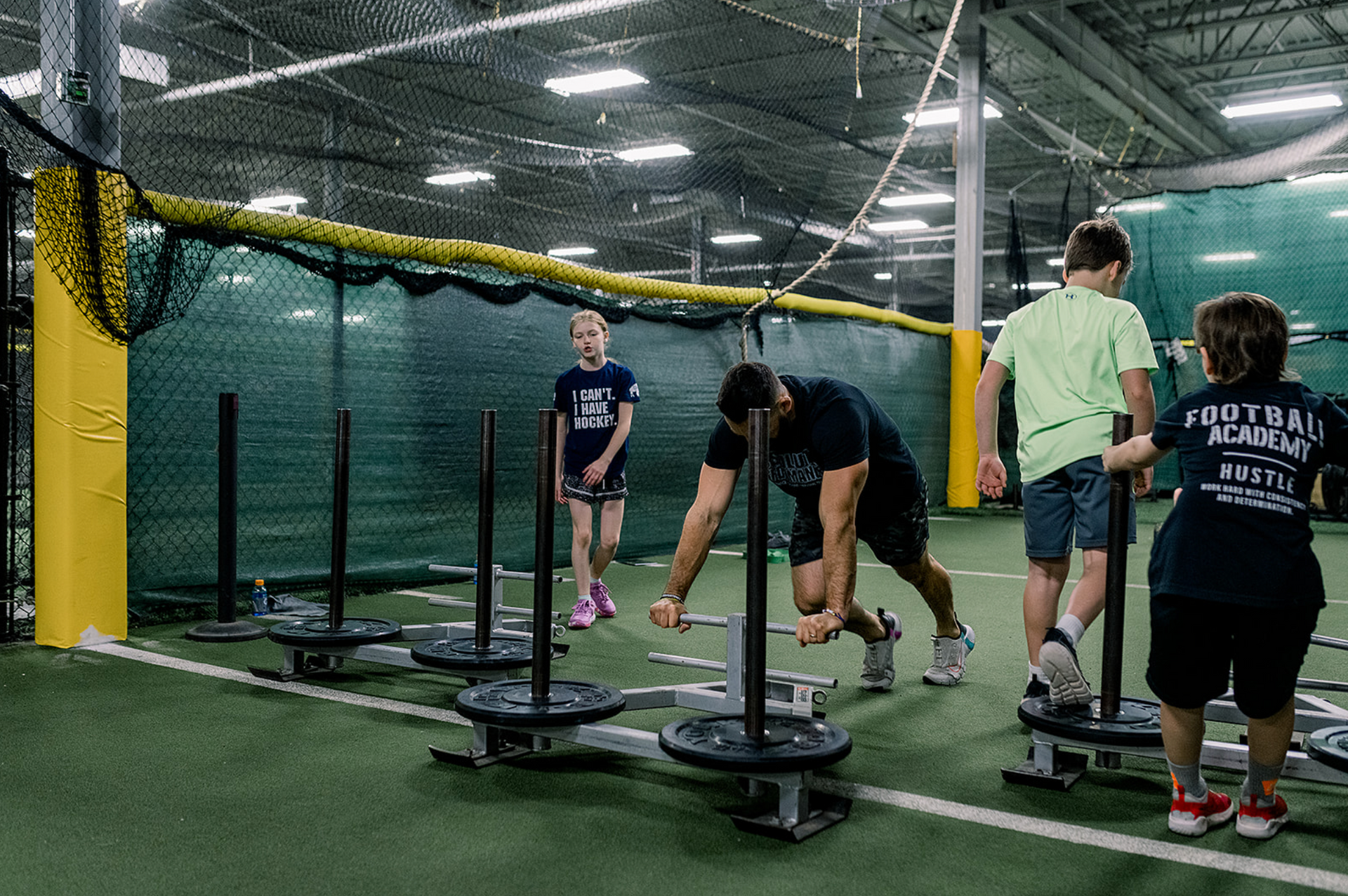 People working out indoors on sled pushes in a netted training area