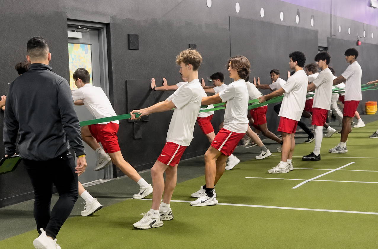 Group exercising indoors, pulling a resistance band in a gym with turf flooring.