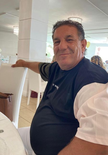 Un uomo con una camicia nera sorride accanto a una colonna bianca in un luminoso ambiente interno.